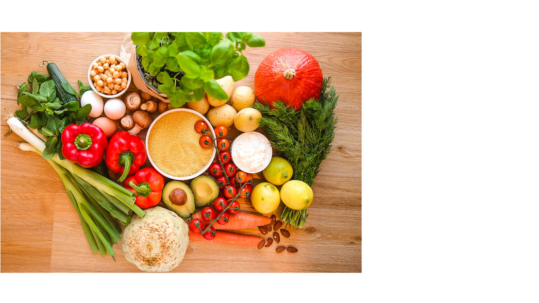 Ein Holztisch mit einer Vielzahl von frischem Gemüse und Obst, darunter Karotten, Tomaten, Zwiebeln, Äpfel, Grünzeug und Ingwer, die zusammen angeordnet sind.
