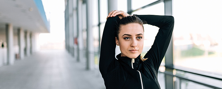 Sport Junge Frau macht Dehnübung. Sie hält ihre Arme über dem Kopf.