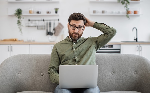 Ein Mann sitzt auf einem Sofa und blickt auf seinen Laptop.